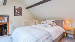 A bedroom with a sloped ceiling, a white bed with patterned pillows, a bedside table with a lamp, and a radiator.