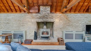 A stone fireplace with a wood-burning stove, flanked by two air vents, in a room with a stone wall and wooden beams. - Barns Lee, Eastcourt - sleeps 9 guests in 5 bedrooms (Eastcourt)
