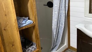 Un baño con una estantería de madera, cortina de ducha y lavabo blanco.