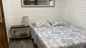 Una habitación pequeña con una cama individual, una colcha estampada, una mesita de noche con lámpara y un espejo en la pared.