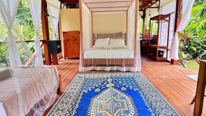 Una cama con dosel, una terraza de madera y un tapete azul estampado.