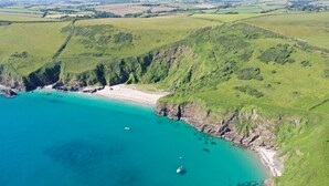 Luchtbeeld van een kustgebied met een strand, kliffen en helder turquoise water.