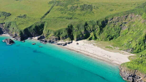 Luchtbeeld van een kustlandschap met een strand, kliffen en een heldere blauwe zee.