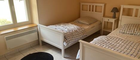A small, clean room with two single beds, a nightstand with a lamp, and a radiator near the window.
