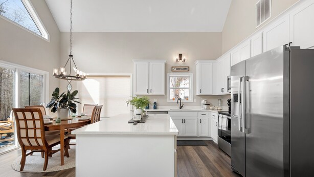 Una cocina moderna con armarios blancos, un refrigerador de acero inoxidable grande y un comedor con sillas de madera y una isla central.