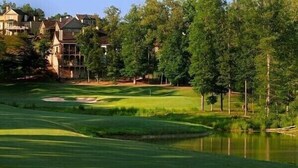 Un campo de golf con un estanque, rodeado de árboles y casas.