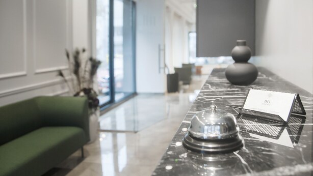 A modern reception area with a marble counter, a green sofa, and a vase. - H41 Luxury Suites (Belgrade)