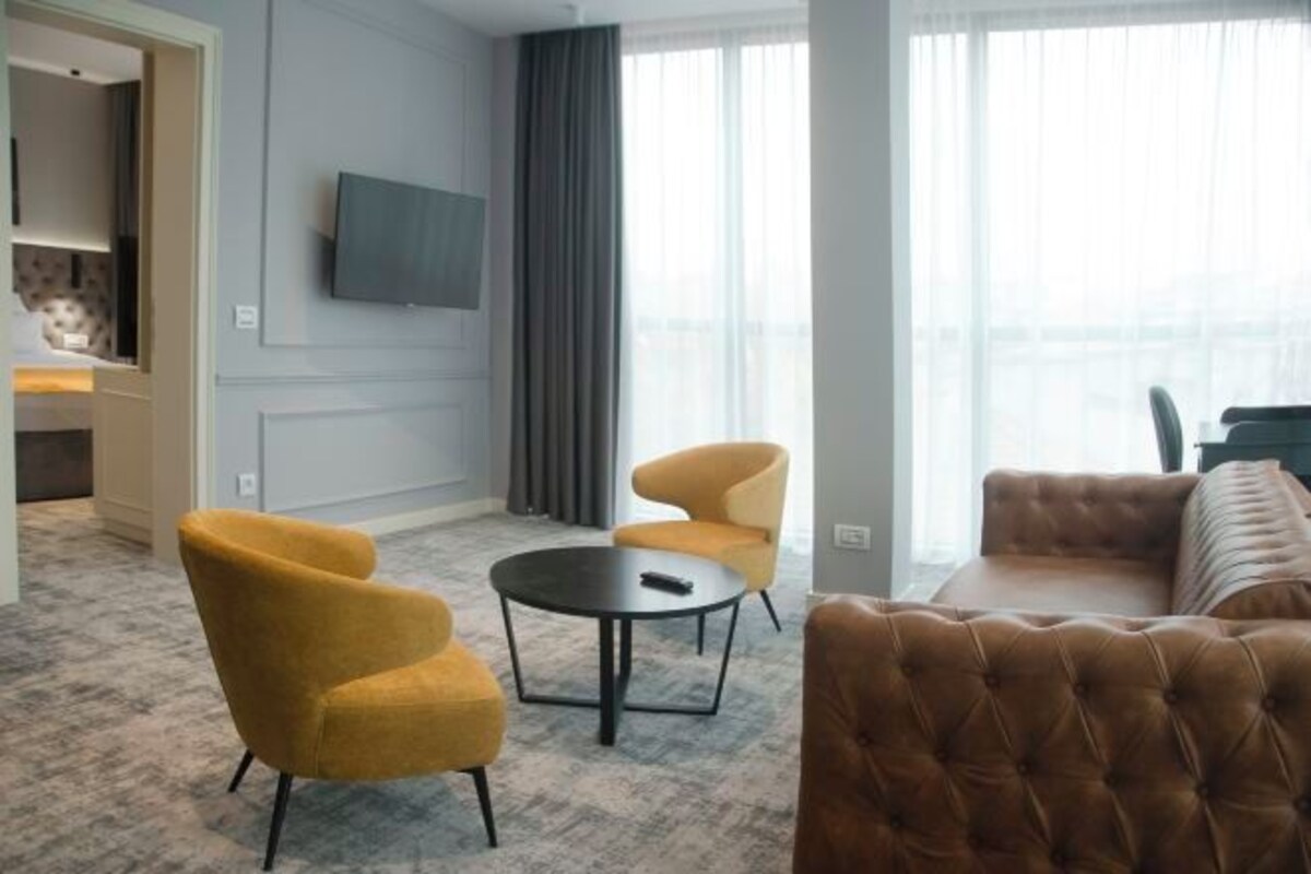 A modern hotel room with a sofa, two armchairs, a small round table, and a TV mounted on the wall.
