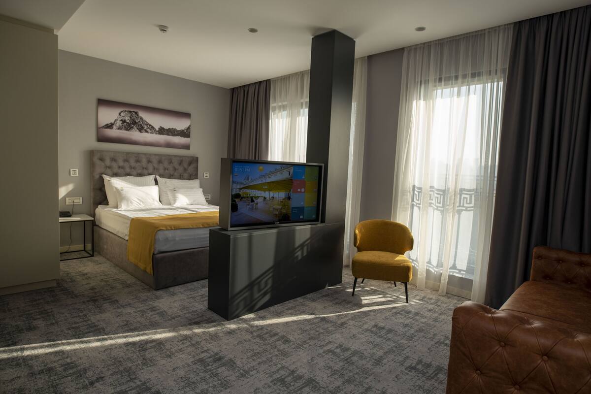 A hotel room with a bed, a TV, a sofa, and a chair.