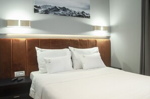 Habitación de hotel con cama, dos almohadas, mesita de noche, control remoto y un cuadro colgado en la pared.