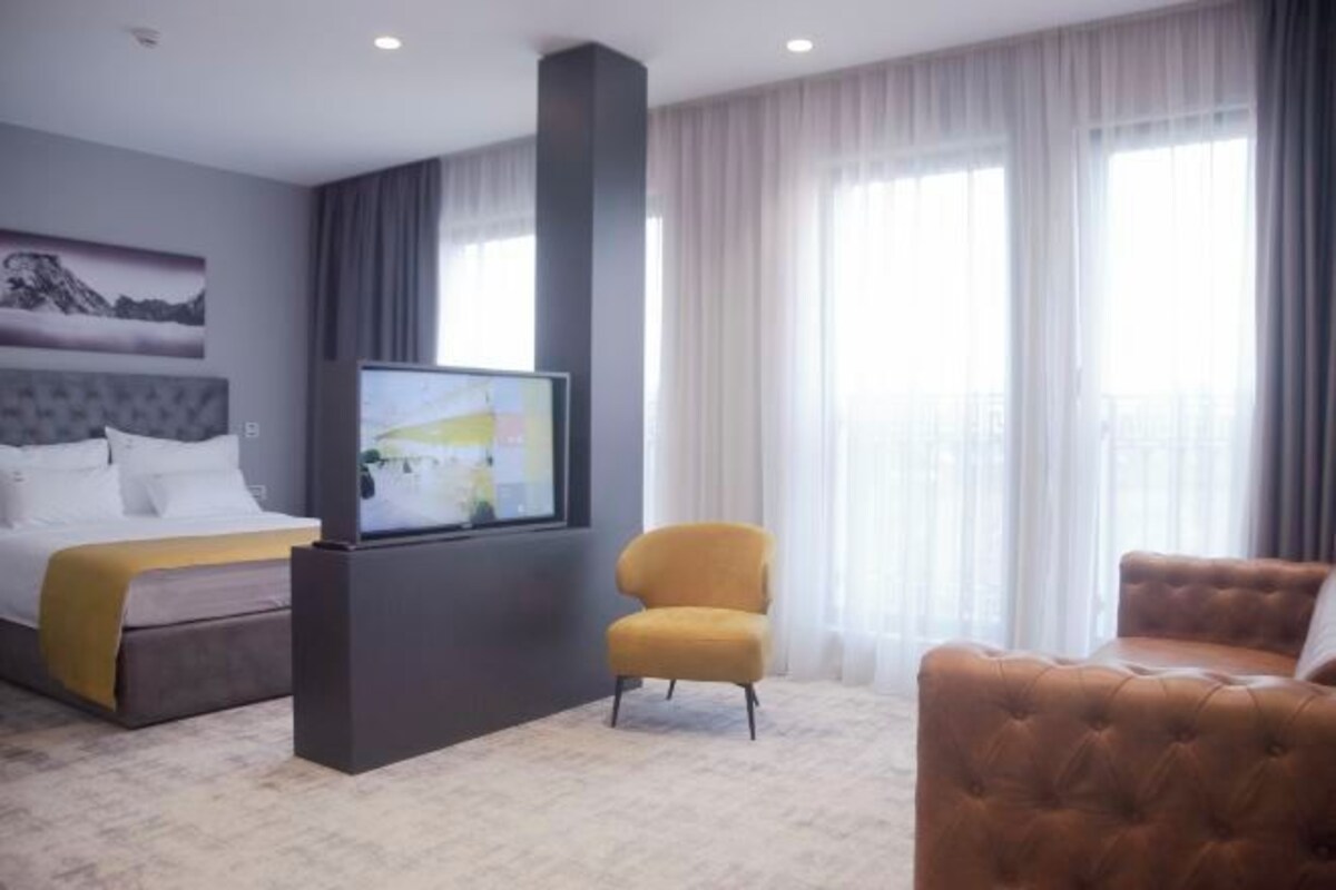 A hotel room with a bed, a television, a yellow armchair, and a brown sofa.