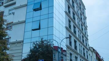 A multi-story building with a modern glass facade, a parking sign, and several parked cars along the street.