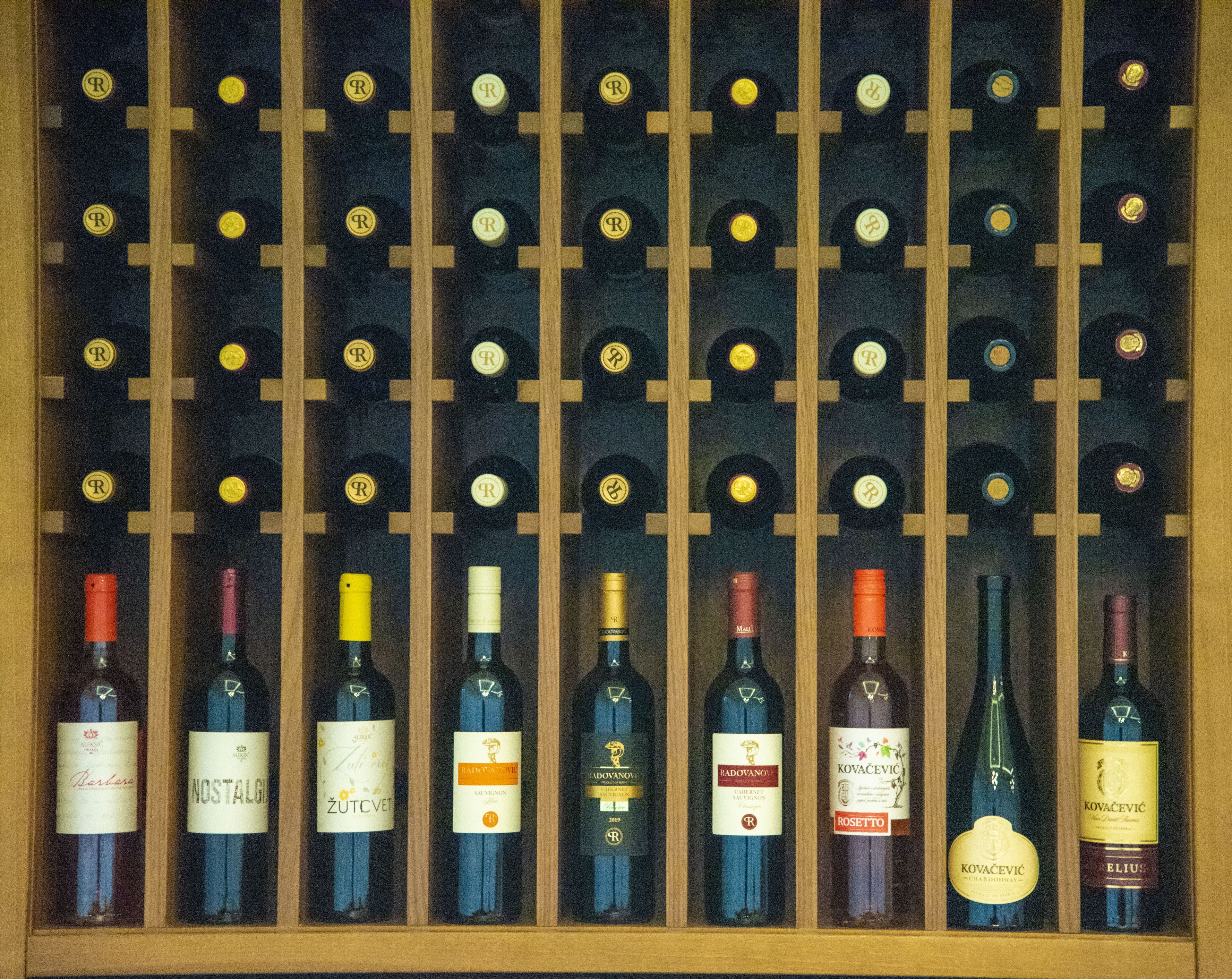 Una estantería para vinos con botellas de diferentes tipos, incluyendo marcas como 'Nostalgia' y 'Kovacevic'.