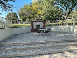 A patio area with a brick fireplace, outdoor seating, and a gravel ground. - Foothills Retreat (Branson)