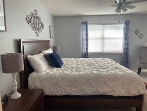 A bedroom with a bed, a nightstand, a lamp, a ceiling fan, and a window with curtains. - Foothills Retreat (Branson)