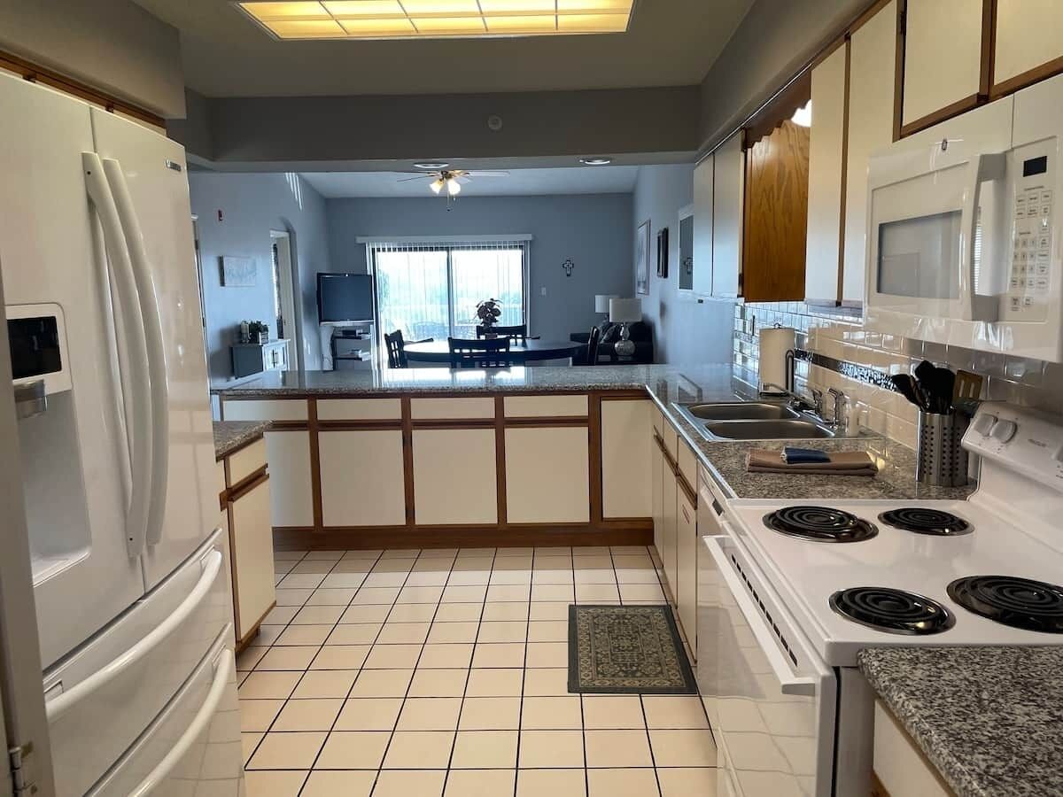 Une cuisine moderne avec un îlot central, des appareils électroménagers blancs et un sol carrelé.