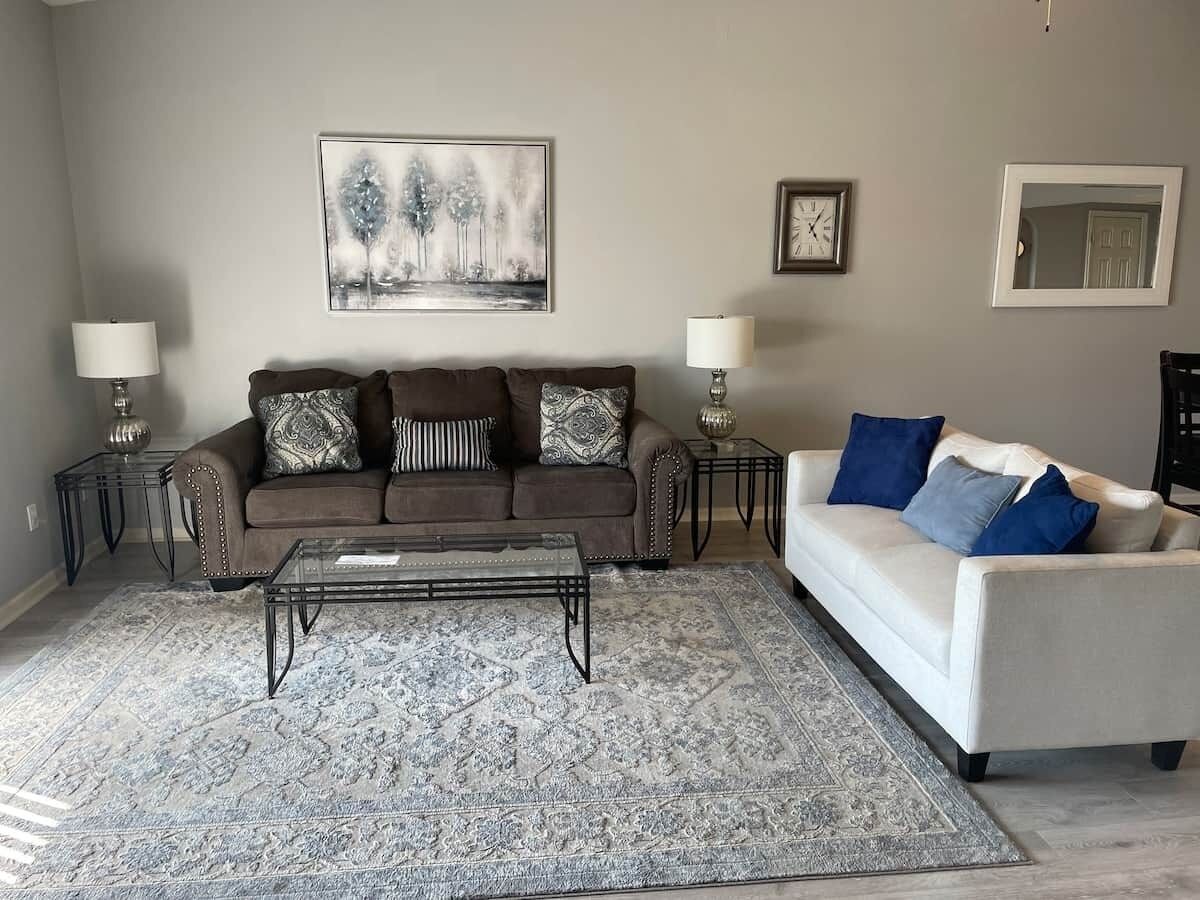 Un salon avec un canapé marron, un canapé blanc, une table basse et un tapis à motifs.