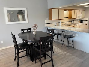 A dining area with a round table and chairs, a kitchen with a microwave and cabinets, and a mirror on the wall.
