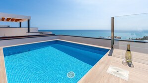 A modern outdoor pool with a clear view of the sea, a wooden deck, and a bottle of champagne. - Penthouse Middle Views | Luxury private terrace pool, sea view (Fuengirola)