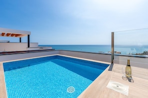 Une piscine sur le toit offrant une vue dégagée sur la mer, une bouteille de champagne et un verre sur la terrasse.
