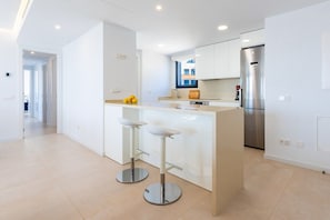 Une cuisine moderne dotée d’un îlot central, d’appareils électroménagers en acier inoxydable et de meubles de rangement blancs.