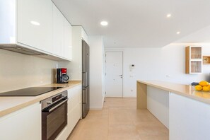 Eine moderne Küche mit weißen Schränken, einem Backofen, einer Kaffeemaschine und einem Kühlschrank.