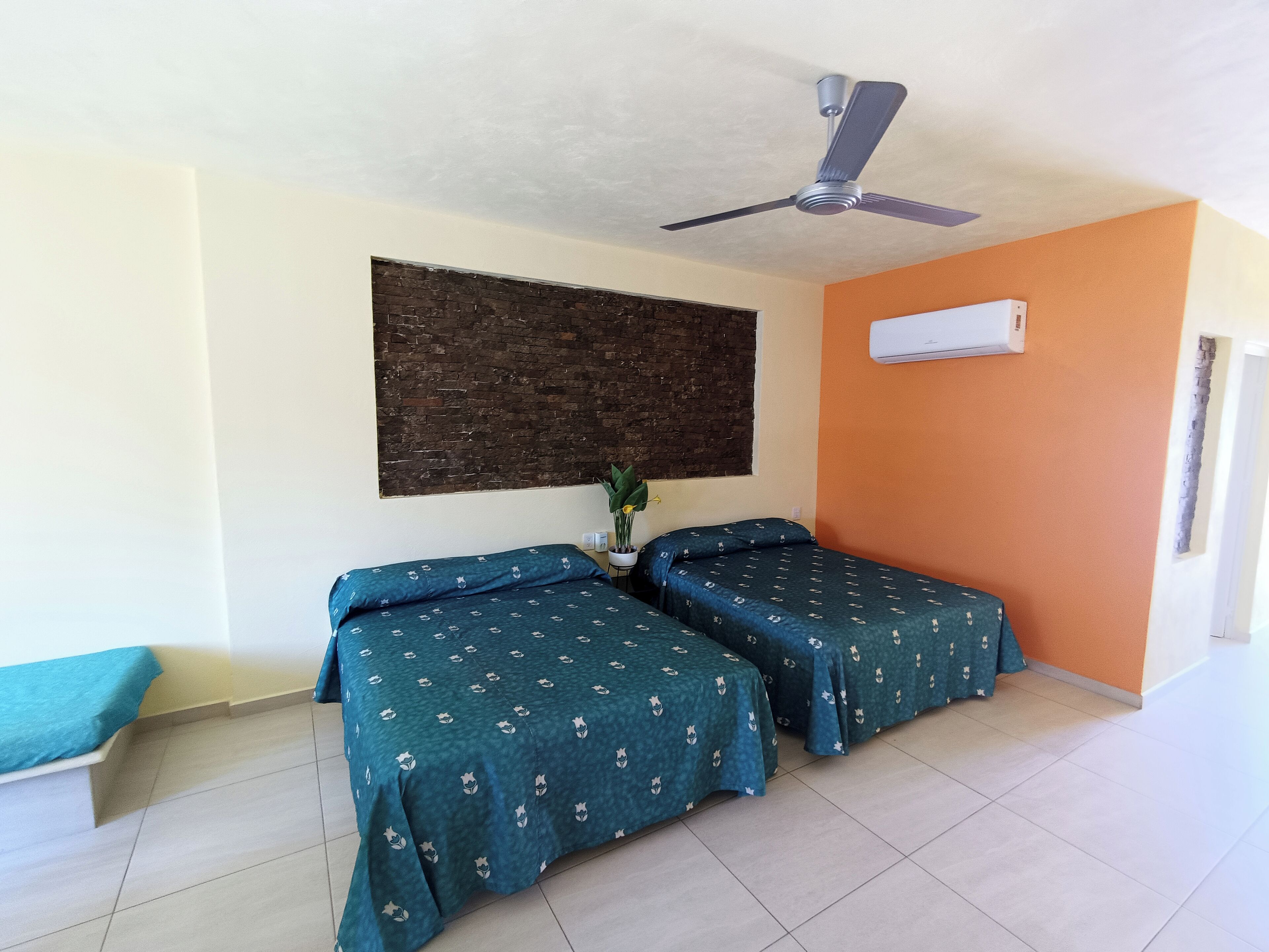 Una habitación con dos camas, ventilador de techo, aire acondicionado y pared de ladrillo.