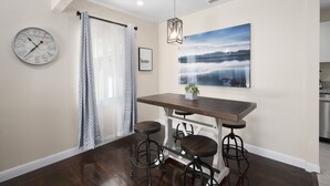 Un coin repas avec une table en bois et des tabourets de bar, une horloge et un tableau encadré au mur.