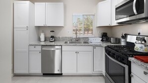 Une cuisine moderne avec des meubles blancs, un lave-vaisselle en acier inoxydable, une cuisinière à gaz et un four à micro-ondes.