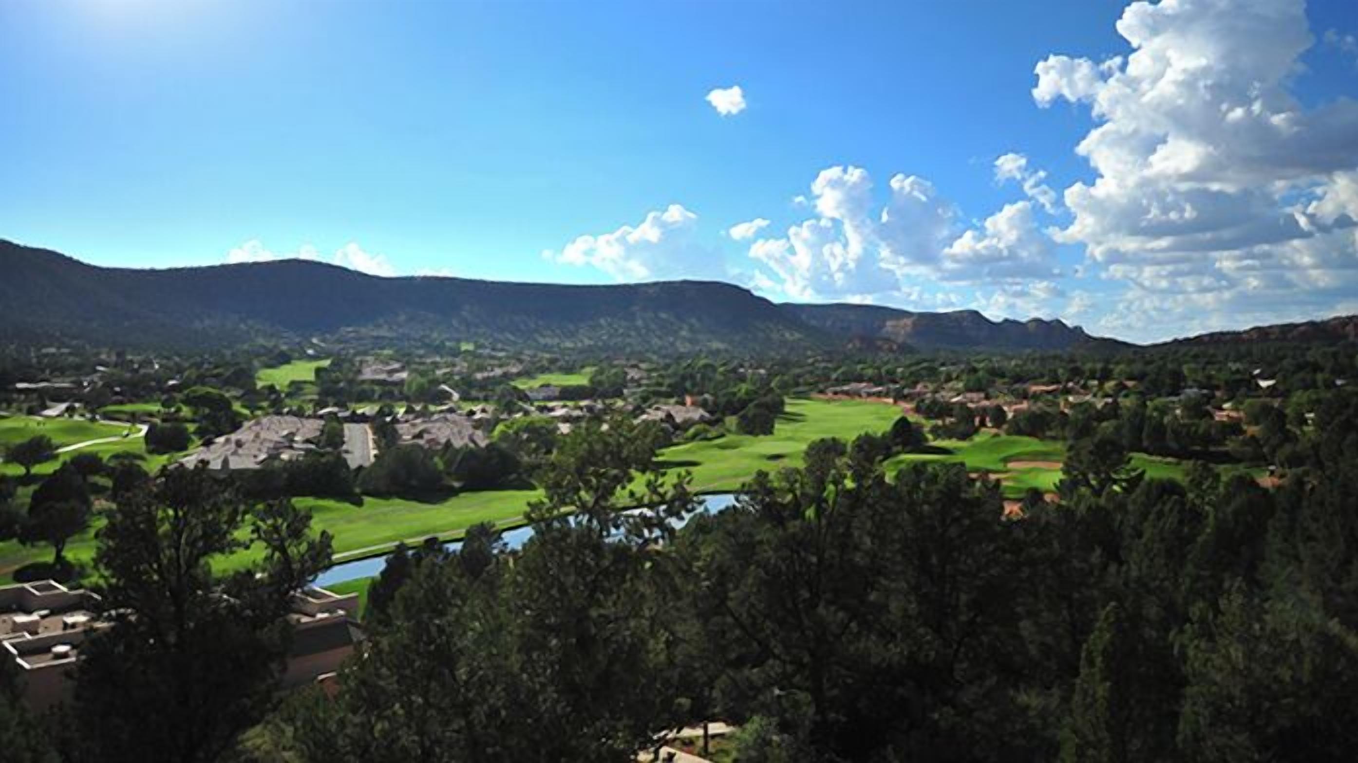 Una vista panorámica de un valle con un río, campos verdes y una cadena montañosa al fondo.
