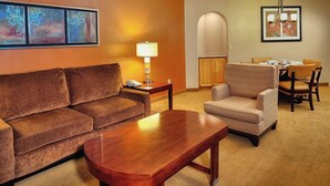 A hotel room with a brown sofa, a wooden coffee table, a patterned armchair, a dining table with chairs, and a lamp. - Sedona | Desert Golf Escape | Trails, Greens & Resort Pools (Sedona)
