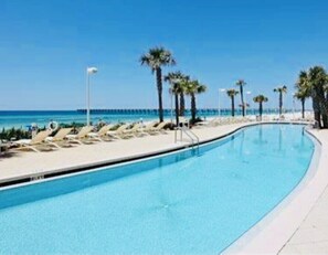 A swimming pool with lounge chairs and palm trees, a pier in the background, and a clear blue sky. - OCEAN FRONT PROPERTY next to Pier Park with pools, tiki bars (Panama City)