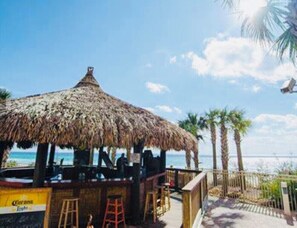 A beachside bar with a thatched roof, palm trees, and a view of the ocean. - OCEAN FRONT PROPERTY next to Pier Park with pools, tiki bars (Panama City)