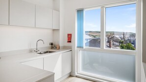 Ett modernt kök med vita skåp, en diskho i rostfritt stål och ett fönster med utsikt över ett bostadsområde.