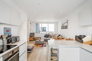 A modern kitchen with white cabinetry, a built-in oven, and a dining area with a wooden table and chairs.