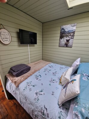A bedroom with a bed, a television, a wall-mounted picture, and a wooden sign. - Stunning 1-bed Shepherd hut (Holyhead)