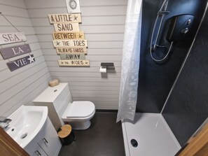 A compact bathroom with a white toilet, a sink, and a shower. There are decorative signs on the wall and a towel rack. - Stunning 1-bed Shepherd hut (Holyhead)