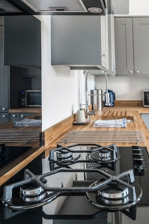 A modern kitchen with a gas stove, wooden countertop, and stainless steel appliances.