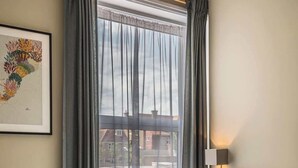 Een netjes opgemaakt bed met witte lakens en opgevouwen handdoeken, een hoofdbord, een bedlamp en een ingelijst beeld aan de muur.