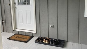 A front door with a mailbox, a doormat, and a shoe rack with boots and slippers.
