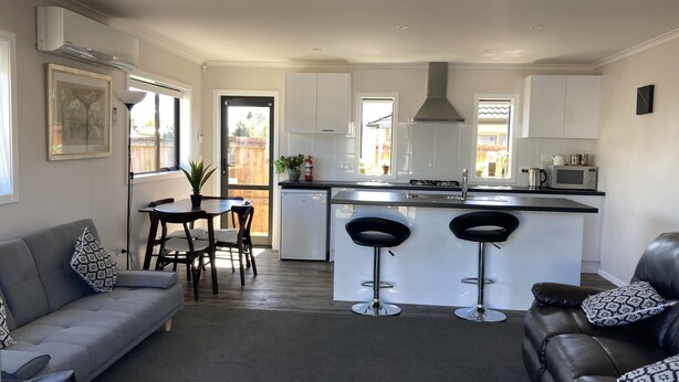 A modern kitchen with a central island, bar stools, and a dining area with a sofa and chairs. - Very modern, new, clean, 3 Bedroom home 2 bathroom (Tūrangi)