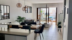 A modern kitchen with a central island, dining area with chairs, and a view through large sliding doors to an outdoor patio.