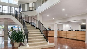 A spacious lobby with a curved staircase, a reception desk, and a large potted plant. - Orlando | Friends Orlando Getaway | 3BR Sleeps 8 (Orlando)