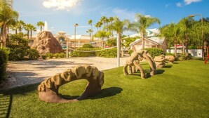 A landscaped area with artificial rock formations, a volleyball net, and palm trees. - Orlando | Friends Orlando Getaway | 3BR Sleeps 8 (Orlando)