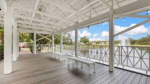 A covered outdoor area with wooden flooring, white railings, and benches. - Orlando | Friends Orlando Getaway | 3BR Sleeps 8 (Orlando)