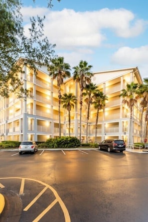 A multi-story hotel with balconies, palm trees, and a parking lot.
