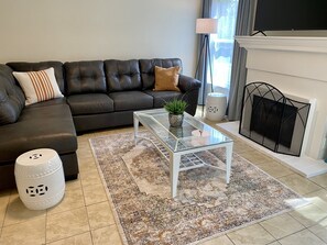 Una sala moderna con un sofá de cuero, una mesa de centro de vidrio, un tapete estampado, un cesto de basura blanco y una chimenea.
