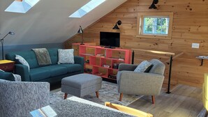 Una sala de estar estilo loft con techo inclinado, un televisor, un mueble de entretenimiento rojo y un comedor con encimera de granito.