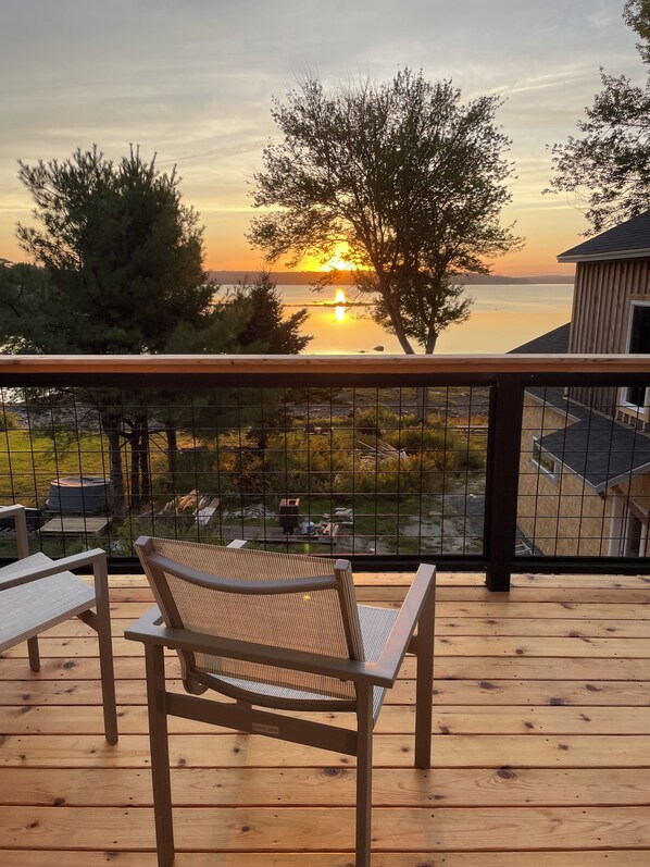 A wooden deck with two chairs, a railing, and a view of the sunset over a body of water.
