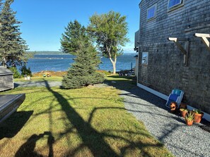 A wooden cabin with a gravel driveway, a lawn, and a view of the water.